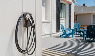 wall-mounted EV charger with a coiled cord and outdoor patio furniture in the background.