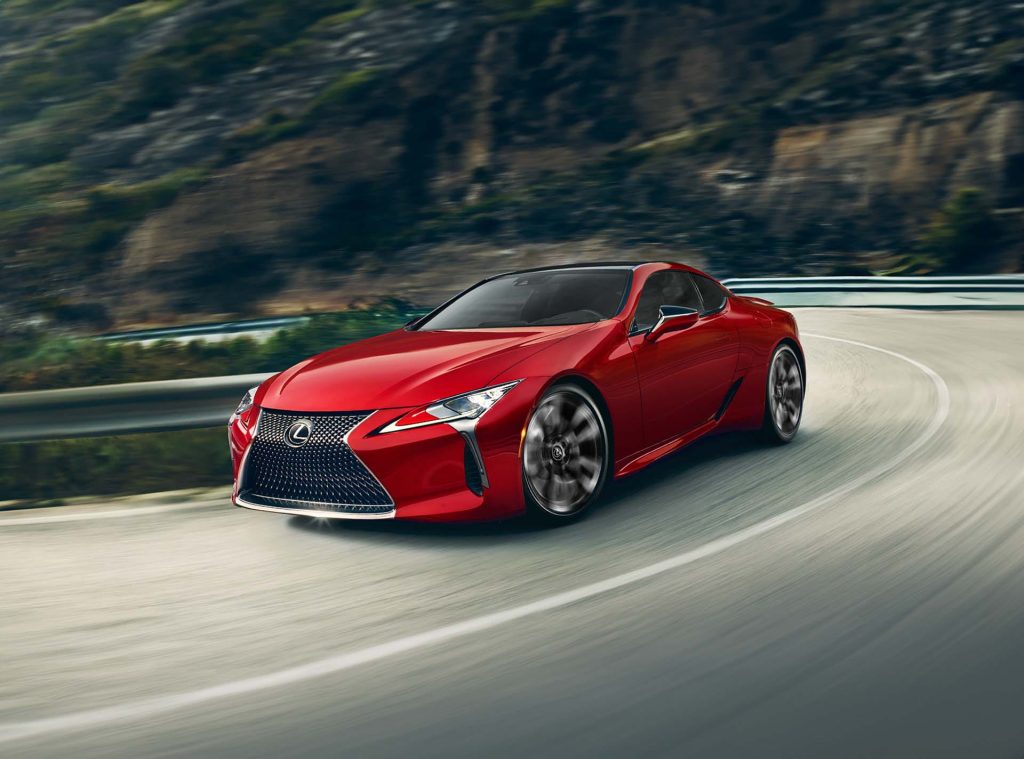 Red Lexus LC 500 sports coupe driving on a winding mountain road with motion blur.