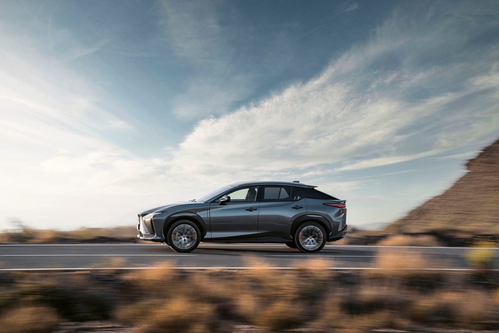 Gray Lexus RZ electric SUV driving on an open desert highway with motion blur and wide sky.